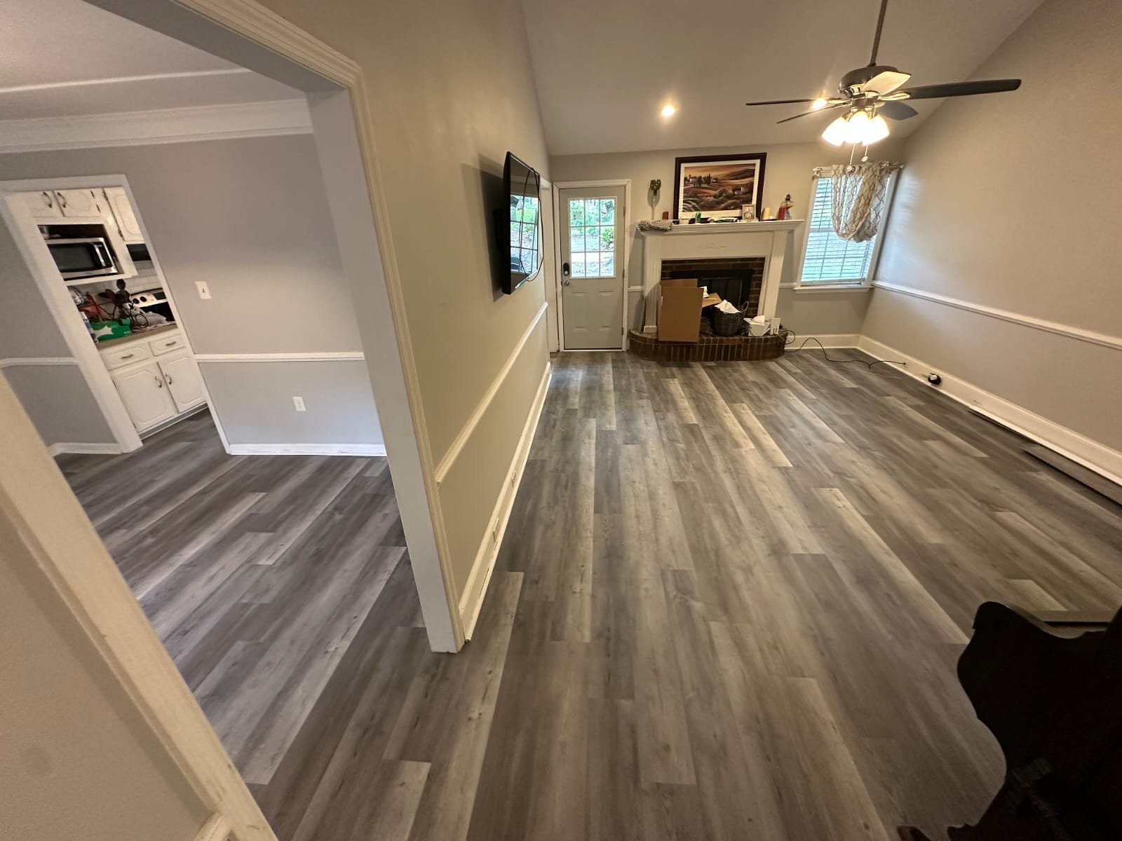 Empty living room with gray plank flooring, a fireplace and a ceiling fan